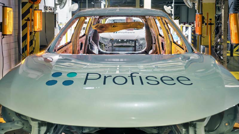 A car with the Profisee logo branded across the hood rolls off the production line at a car manufacturing plant.